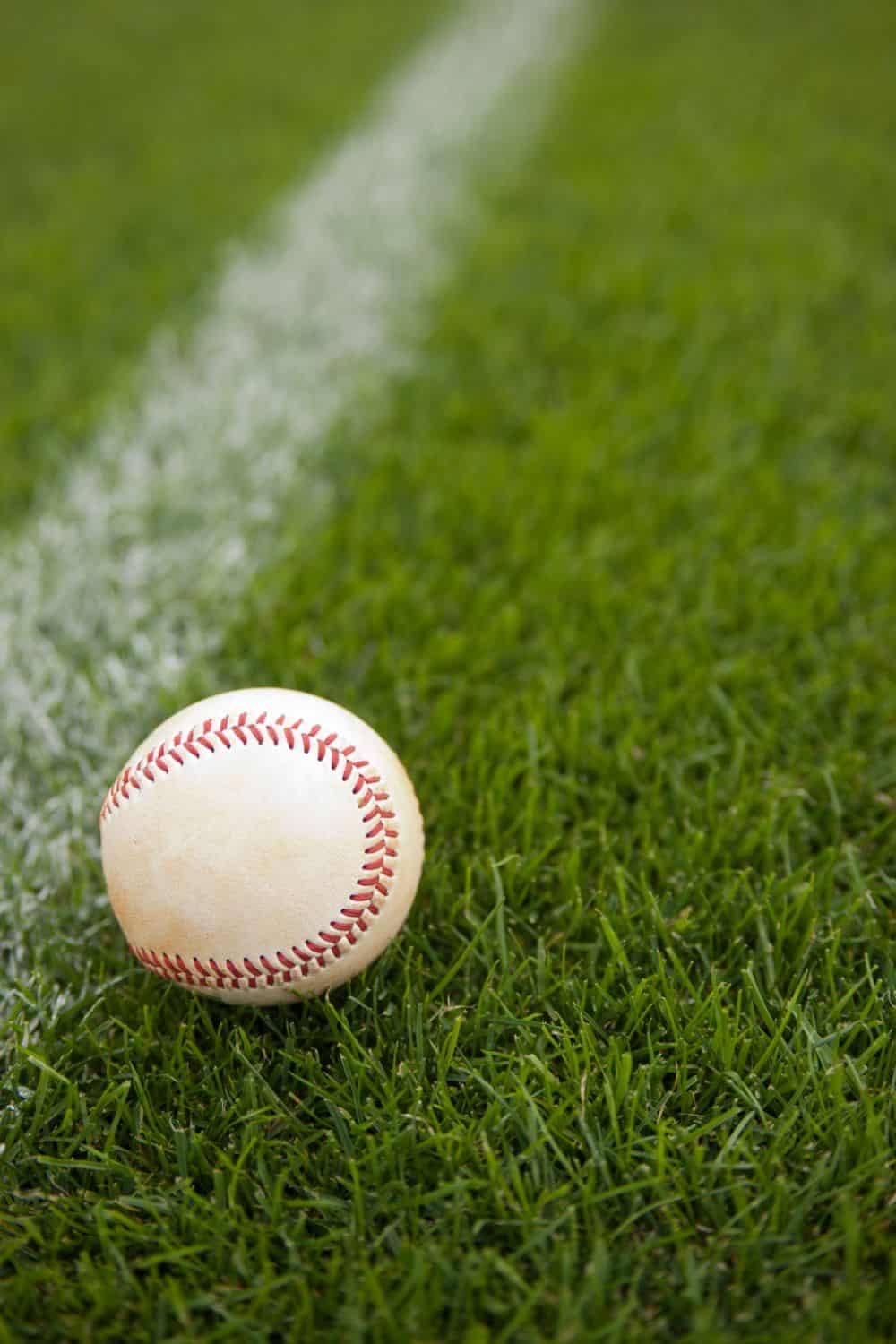 A baseball rests on vibrant green artificial turf near a white chalk foul line on the sports field.